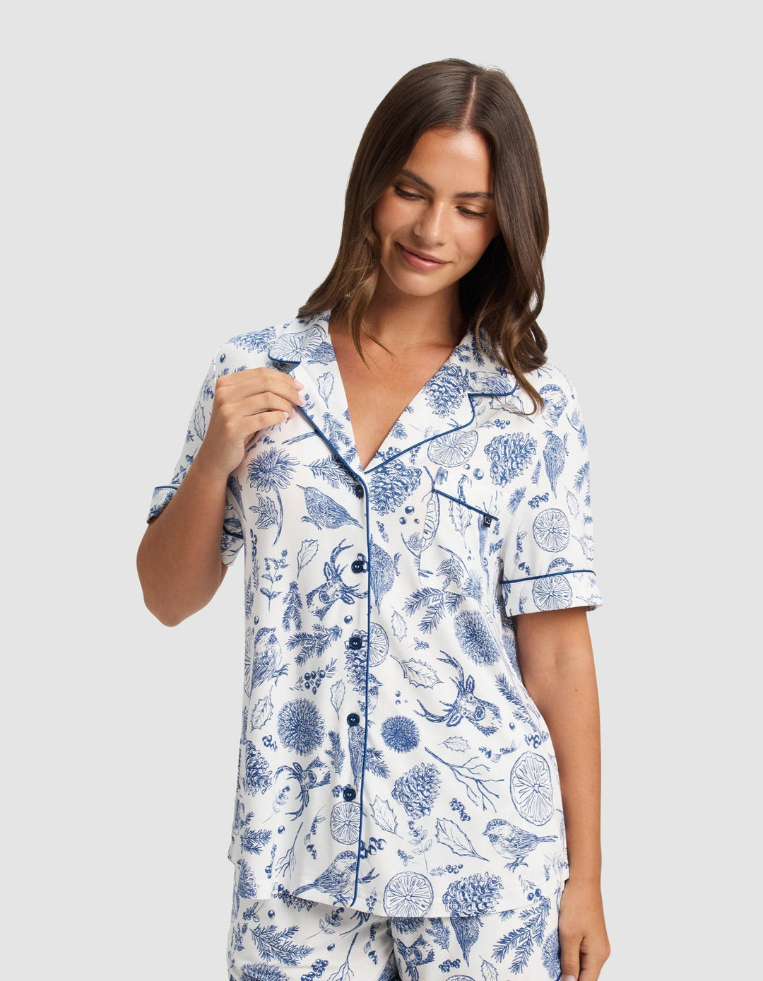 A woman smiles wearing the Cozy Earth Women's Bamboo Stretch-Knit Short Sleeve Pajama Top and matching shorts featuring a blue botanical print on a white background.|Color:Winter Toile Pacific